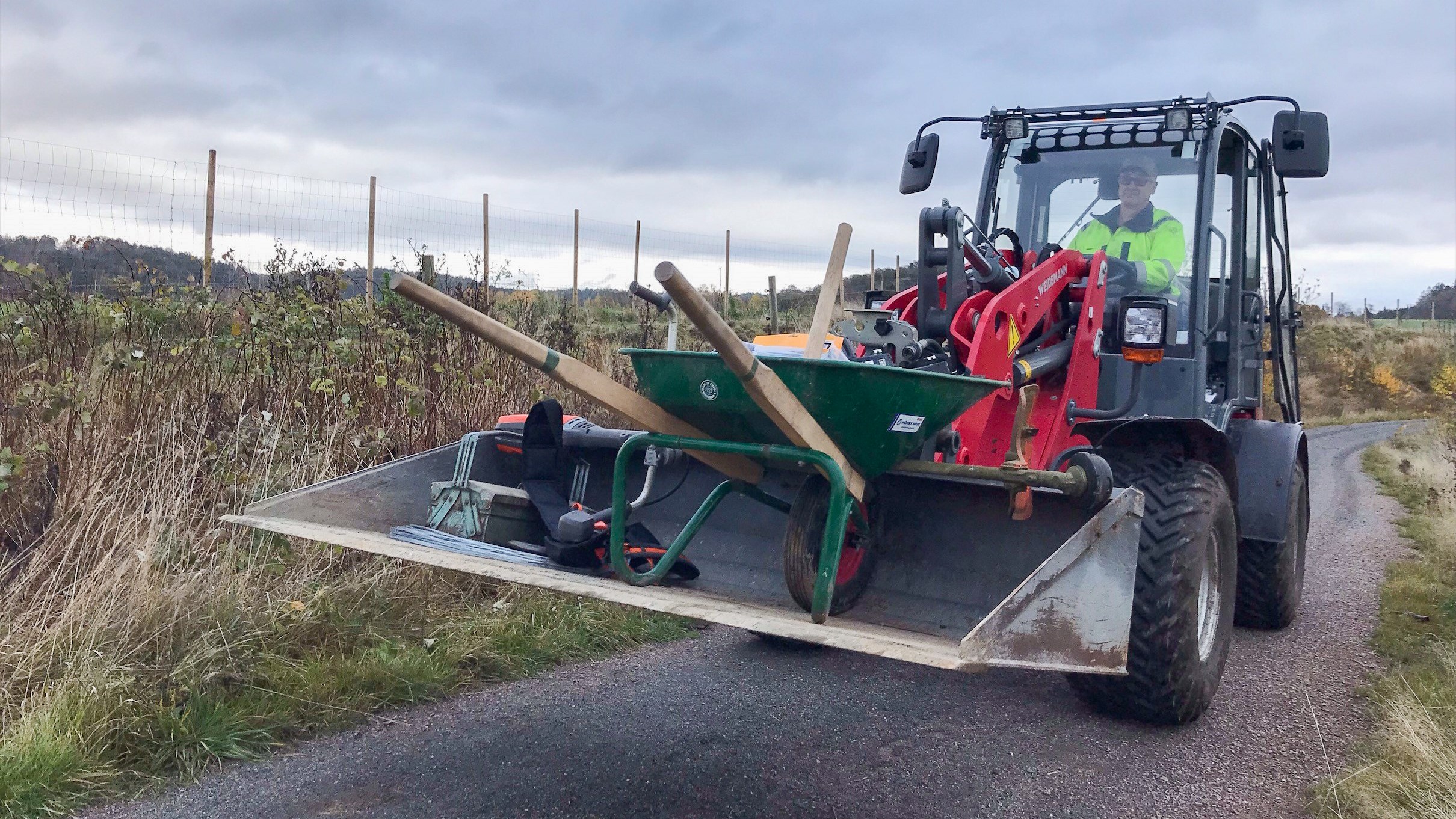 Maskin kör redskap och skottkärra i skopa på en landsväg