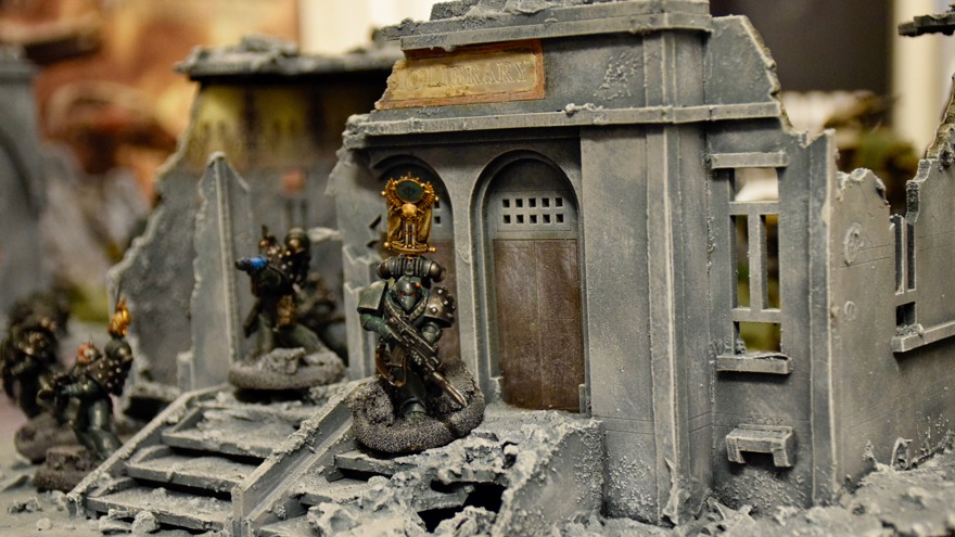 En spelfigur med vapen står utanför ett raserat bibliotek.