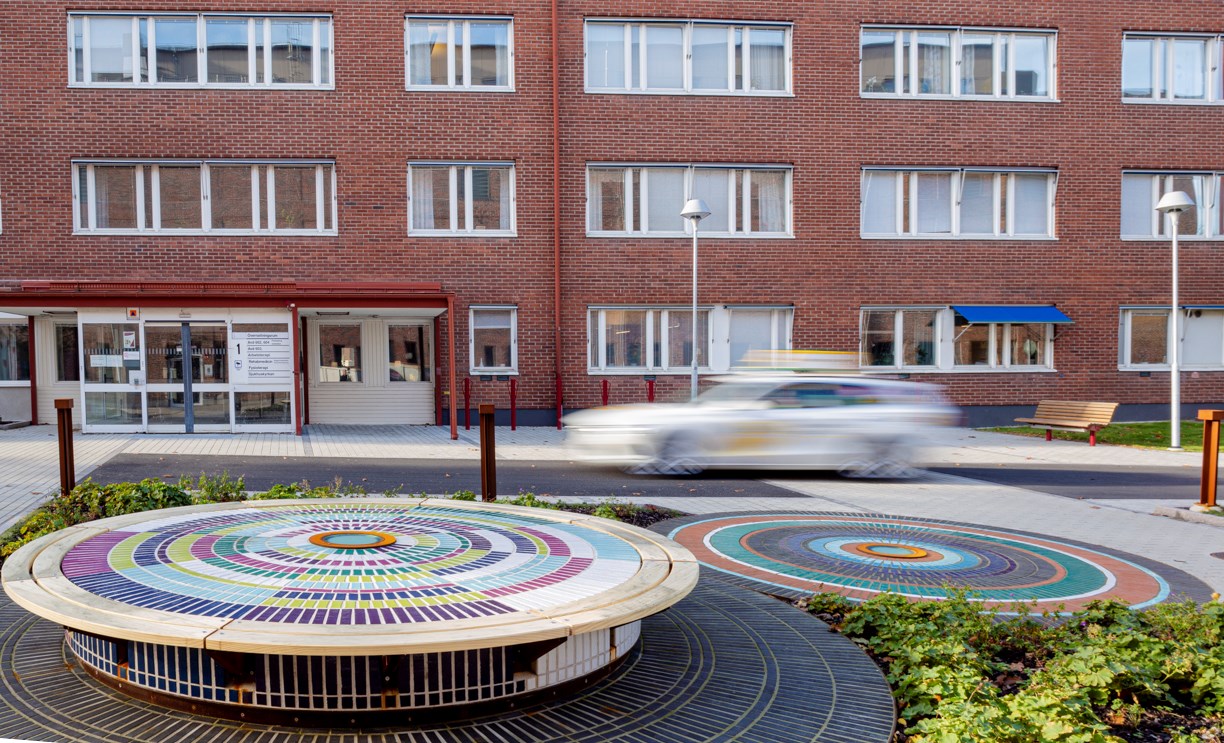 Rundlar med färgade kakelplattor. I bakgrunden en röd tegelbyggnad och en taxibil.