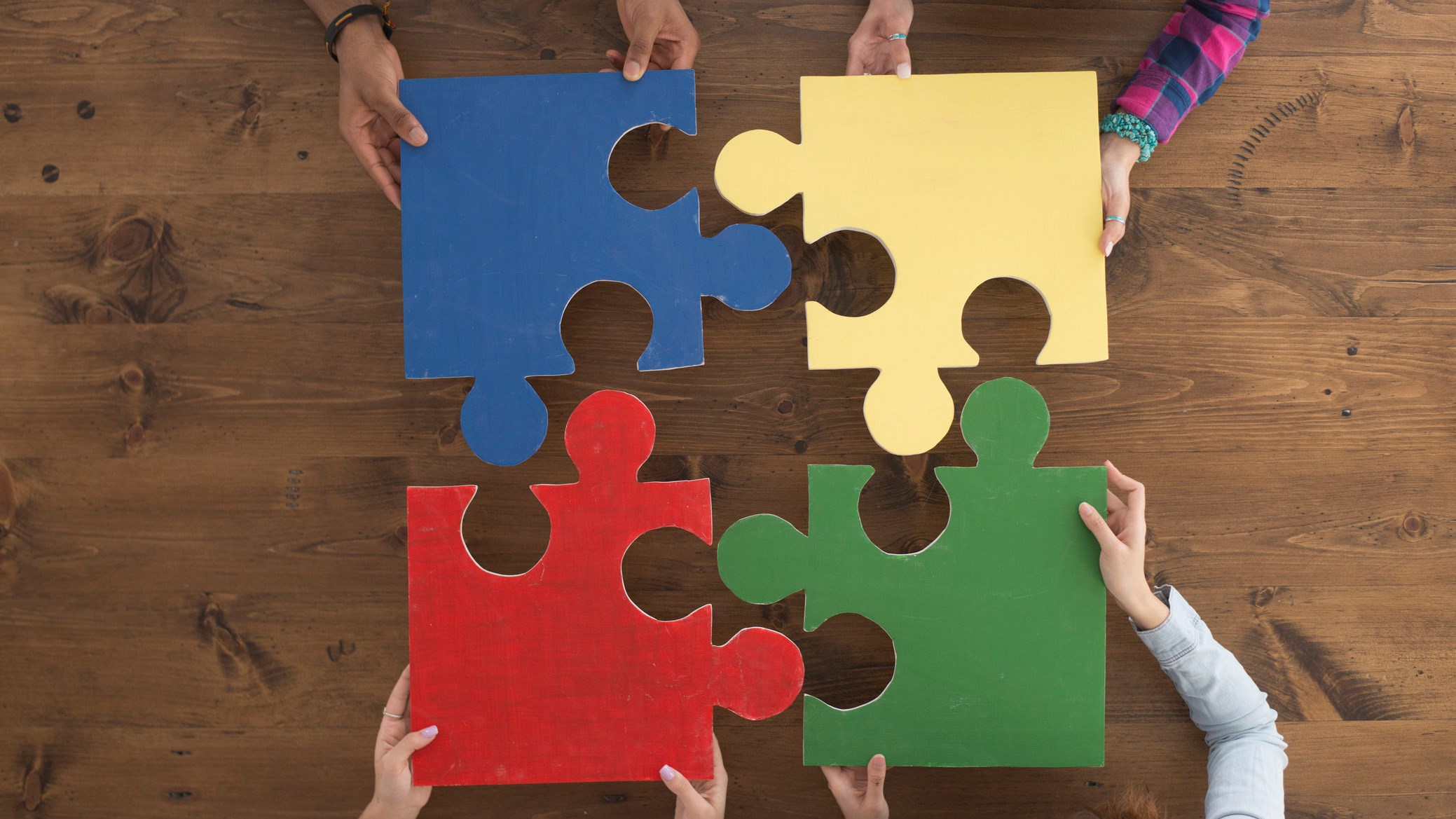 A multi-ethnic group of college age students are putting together large puzzle pieces.