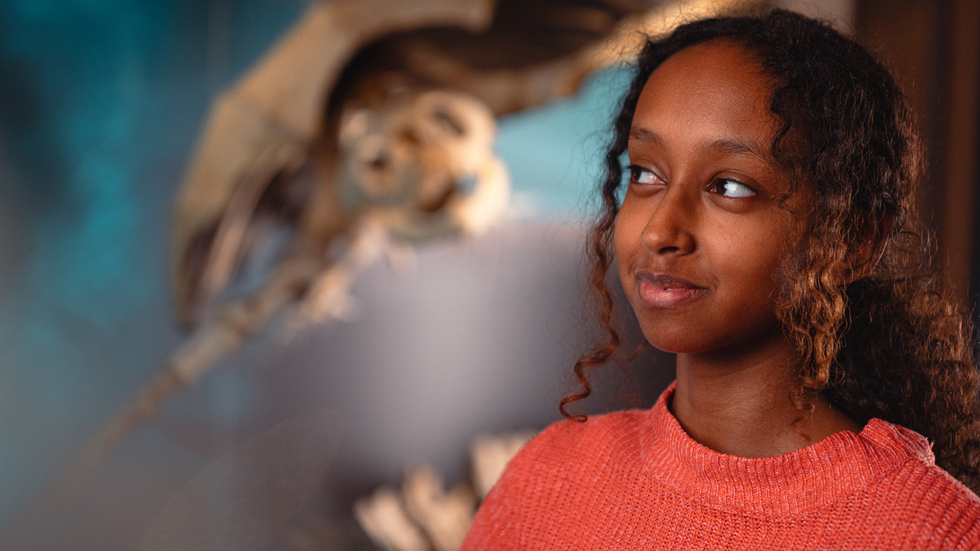 Ett barn till höger i bild syns titta på något till vänster som inte syns, i bakgrunden ett skelett i oskärpa av något djur 