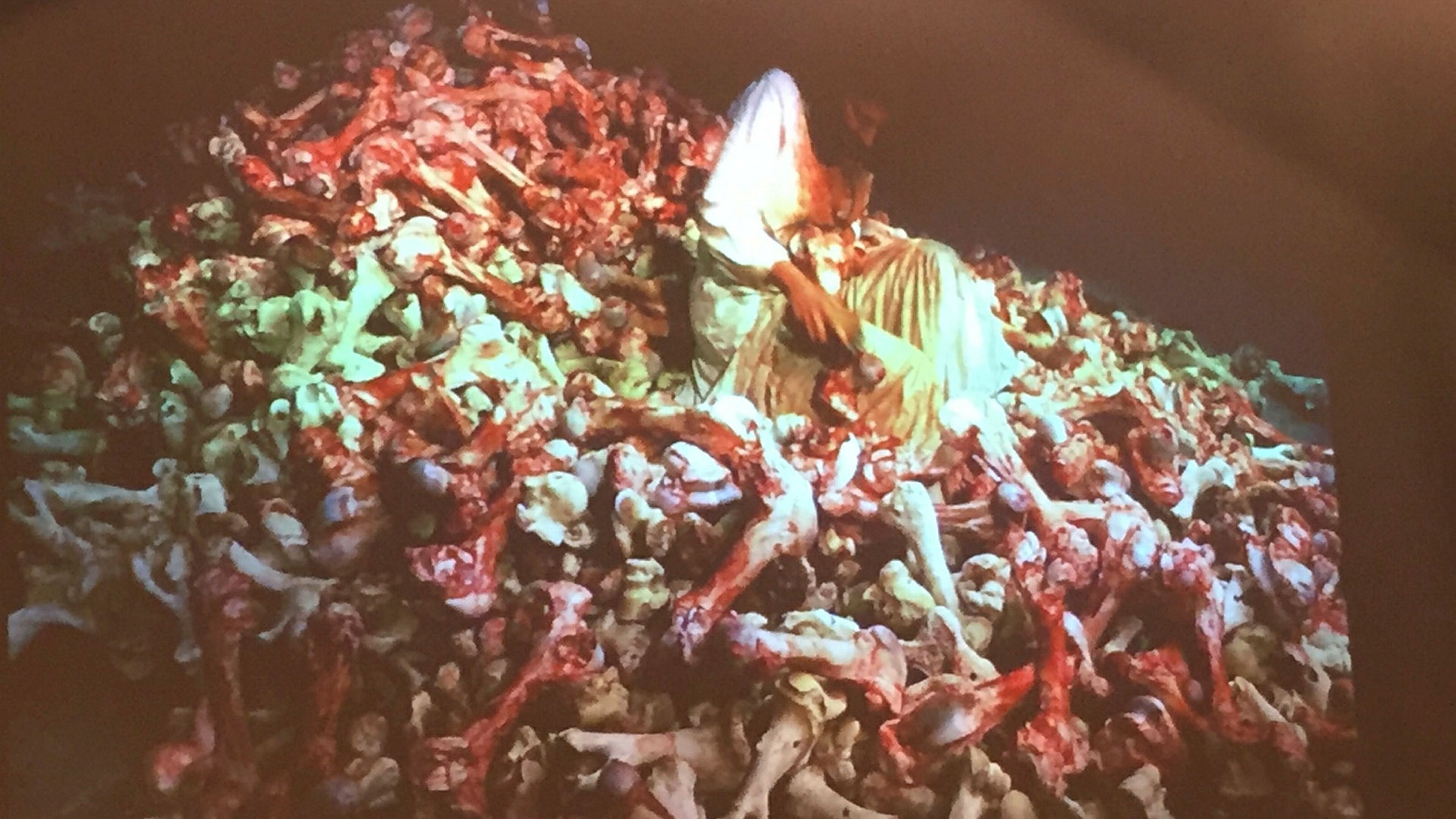 En människa i en vit särk sitter på en hög med blodiga ben.