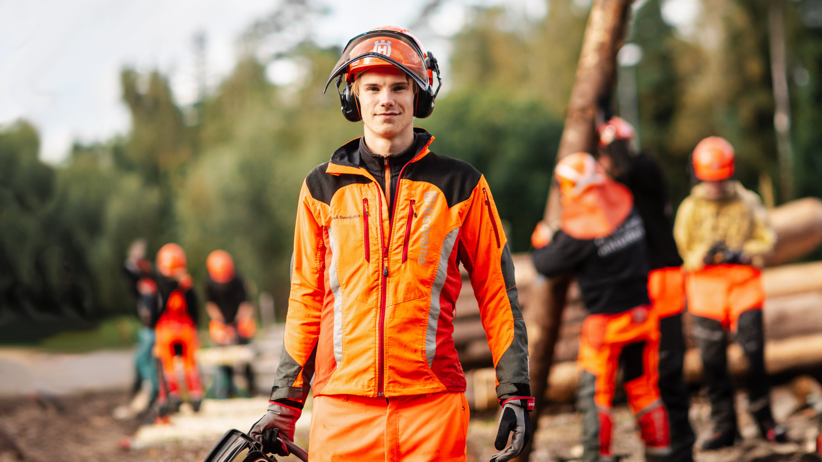 Elev med hjälm och orangea skyddskläder håller i motorsåg
